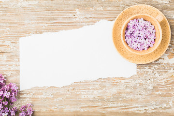 A piece of torn paper and a cup with lilac flowers on an old board