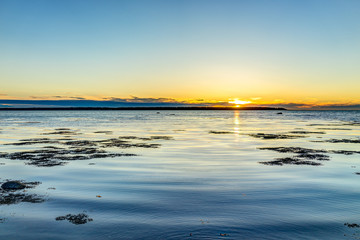 Sunset in Rimouski, Quebec by Saint Lawrence river in Gaspesie region of Canada with sand, seaweed in water and view of coast