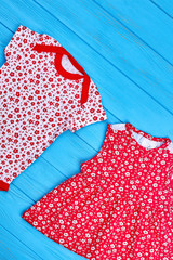 Toddler girl summer cotton clothes. Infant baby girl brand summer clothing in red tone, blue wooden background. Patterned organic clothes for newborn girl.