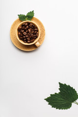 Coffee cup filled with coffee beans and green fresh leaves