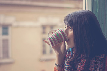 Young woman drinkig coffe by the window in warm home
