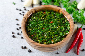 Traditional argentinian chimichurri sauce made of parsley, cilantro, garlic and chili pepper in a wooden bowl. Selective focus, horizontal image © losinstantes