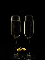 Two glasses and champagne bottle on a black background in New Year's style.