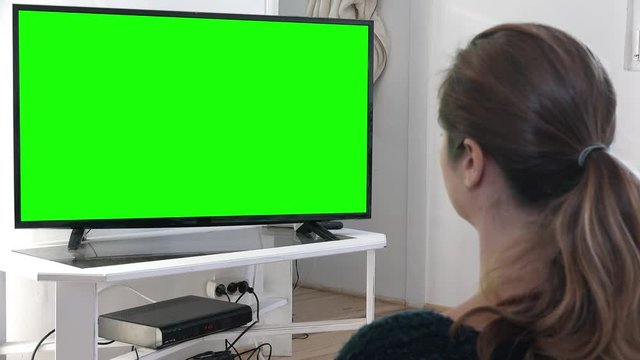 Woman Watching Green Screen Television. Charming young woman watching green screen television at home. Shot behind model shoulders.