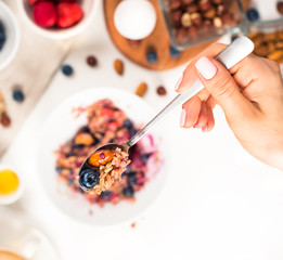 Top view showing hands eating porridge with honey nuts, blueberries on white wooden table selective focus, blurred background Good morning - healthy breakfast background