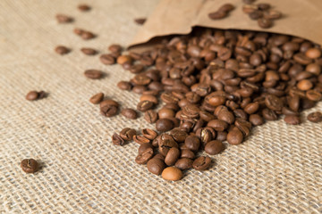 coffee beans spilled out of a paper bag on a linen surface bag