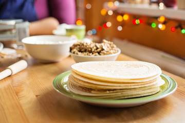 Fototapeta na wymiar Christmas wafers placed on a wooden kitchen table, on a green plate next to a window. Wafers are round, cream color, surrounded by ingredients