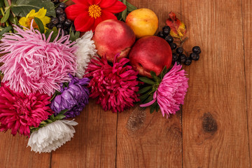 brown wooden background with bright autumn asters, red fruit and chokeberry