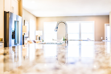 New modern faucet and kitchen room sink closeup with island and granite countertops in model house,...