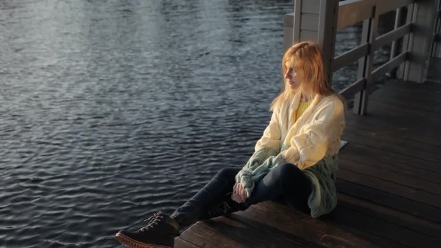 beautiful girl is sitting on the pier near the water