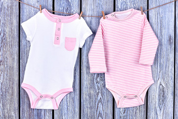 Infants rompers hanging on rope. Kids beautiful clothing drying on clothesline on vintage wooden background.