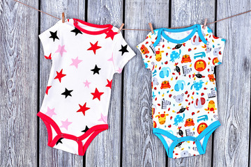 Infants clean apparel hanging on rope. Newborn kids printed bodysuits drying on clothesline on old wooden background.