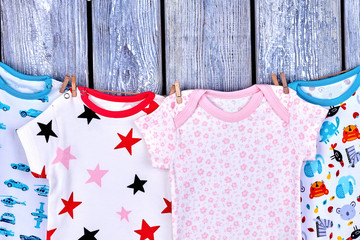 Kids fashion apparel hanging on rope. Collection of infants rompers drying on clothesline on wooden background.