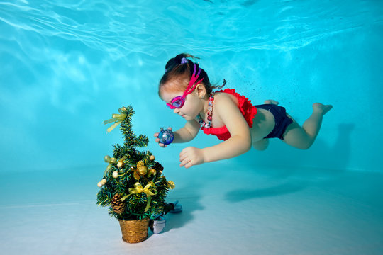 Child underwater in the pool decorates the Christmas tree with Christmas toys. Portrait. Shooting under water. Horizontal orientation