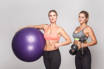 Two activity strong woman looking at camera and posing with gym equipment