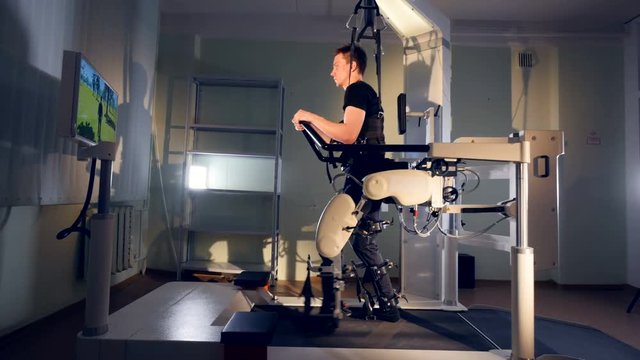 A guy tracks a TV avatar during his exoskeleton training. 