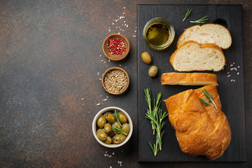 Italian traditional Ciabatta bread with olives, olive oil, pepper and rosemary on a dark stone or concrete background. Selective focus.Top view. Copy space.