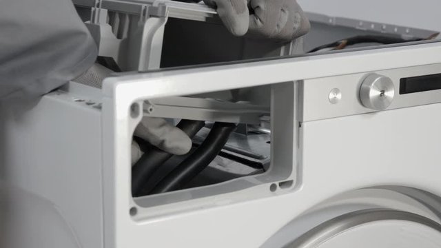 Repairman carefully removing rubber tubes that provide water and are connected to the front side of detergent drawer of the washing machine.