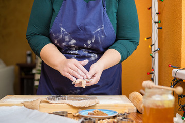 Young caucasian woman standing behind a table, baking for christmas. She is holding raw cookie in the shape of star.
