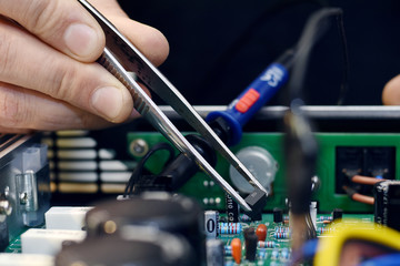 Repairman disassembling smartphone with tweezers. Unrecognizable man holding computer circuit in electronics repair service