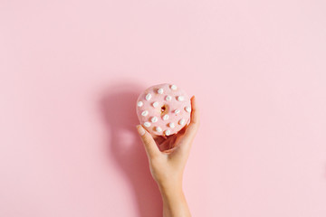 Women's hand holding donut on pink background. Minimal flat lay, top view concept.