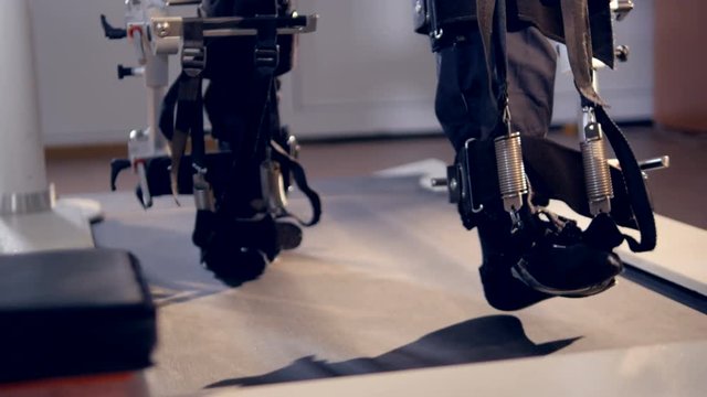 Feet walking on a treadmill inside exoskeleton stirrups. 