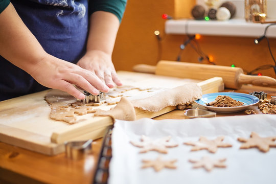 Close up photo of female hands and wooden board with a dough and baking pan with raw cookies in a shape of star. Woman is cutting a christmas cookie with cookie cutter in the shape of star.
