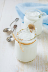 Fresh natural yogurt in a glass jar on  light wooden background. Healthy food.for breakfast. Milk dairy product. Selective focus..