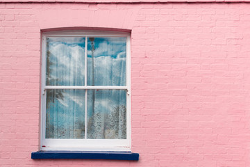 Victorian window with white wooden sash, white curtains and blue balcony on a bright pink painted...