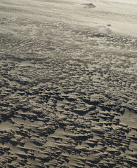 Closeup of a sand beach on a windy day. Little patches of wet sand collect sand in their wake, creating regular, sharp, strips in the main direction of the wind.