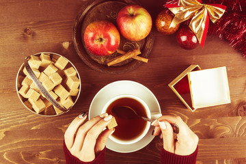 Hands of a girl with a cup of tea on a background of a Christmas composition with toys and fruits