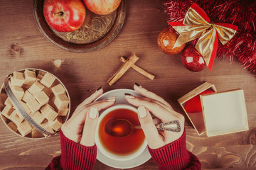 Hands of a girl with a cup of tea on a background of a Christmas composition with toys and fruits