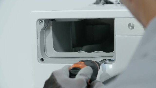 Repairman unscrewing screws of the case that holds detergent drawer. He uses small baterry power drill.