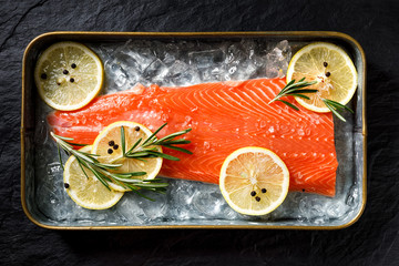 Fresh fish fillet on ice with lemon slices, rosemary, salt and peppercorns, top view