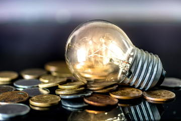 Yellow light bulb on over pile of coins - money, finance, savings concept and idea