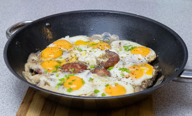 Fried eggs with sausage and chives on a deep black pan closeup
