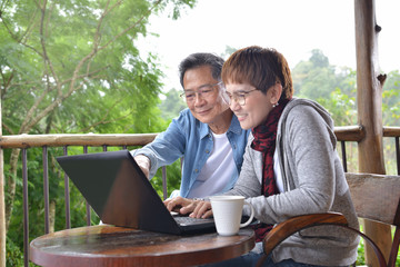 Happy senior couple using laptop computer at home with green garden background