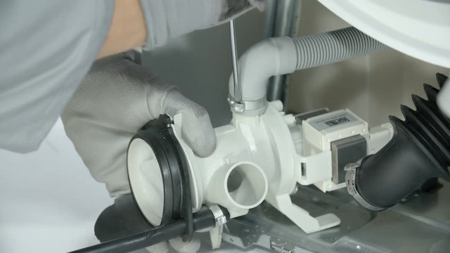 Repairman servicing broken-down washing machine. He is pulling the hose off the drain pump by expanding the clip.