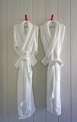 Two white bathrobes hanging in a bathroom