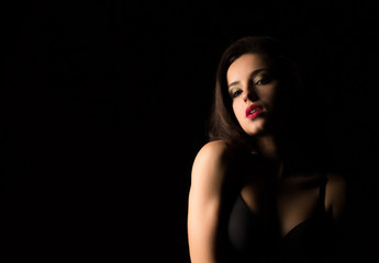 Closeup portrait of seductive woman with bright makeup posing with naked shoulders in the dark
