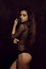 Pretty tanned woman with lush hair in black lingerie posing in the shadow