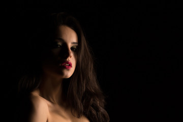Naklejka premium Glamor young woman with bright makeup with naked shoulders posing in the shadow