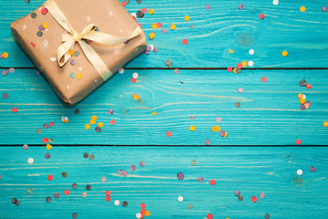 Gift box on turquoise wooden background with confetti.