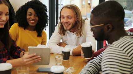 Close up shot of a small diverse group discussing new ideas, looking at the tablet device, while sitting in the cafe and sipping cofee. Indoor shot. - Powered by Adobe