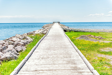 Fototapeta na wymiar Empty long wooden boardwalk with nobody on pier dock quay with gulf of Saint Lawrence river in Gaspesie region of Quebec, Canada with converging lines
