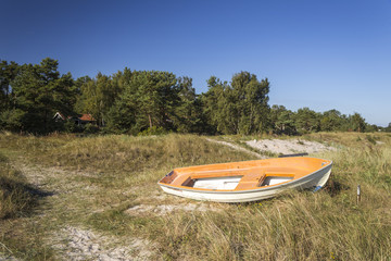 A white and orange boat left on a sandy beach