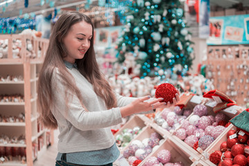 Cheerful happy customer girl choosing gifts for Christmas and New Year. She is taking Christmas tree decorations. difficult decision. Various choice