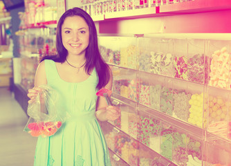 Pretty girl in sweets store picks up candies in   bag