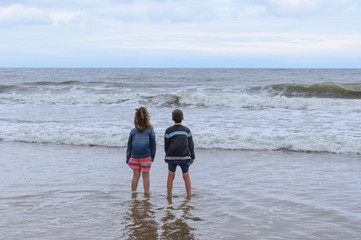 A young girl and boy enjoying the waves at the beach.