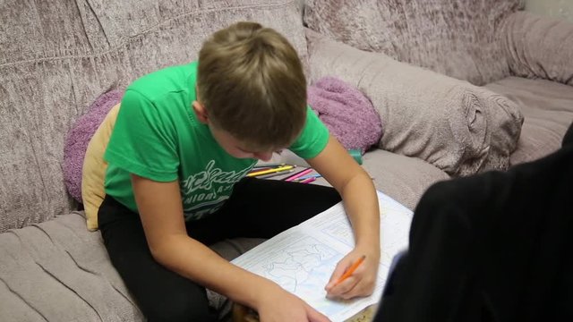 The boy does the school assignment. A boy in a green T-shirt at home at school assignments